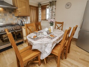 A kitchen with wooden cabinets, a stove, and a dining table set with plates, a croissant, and a vase with flowers.