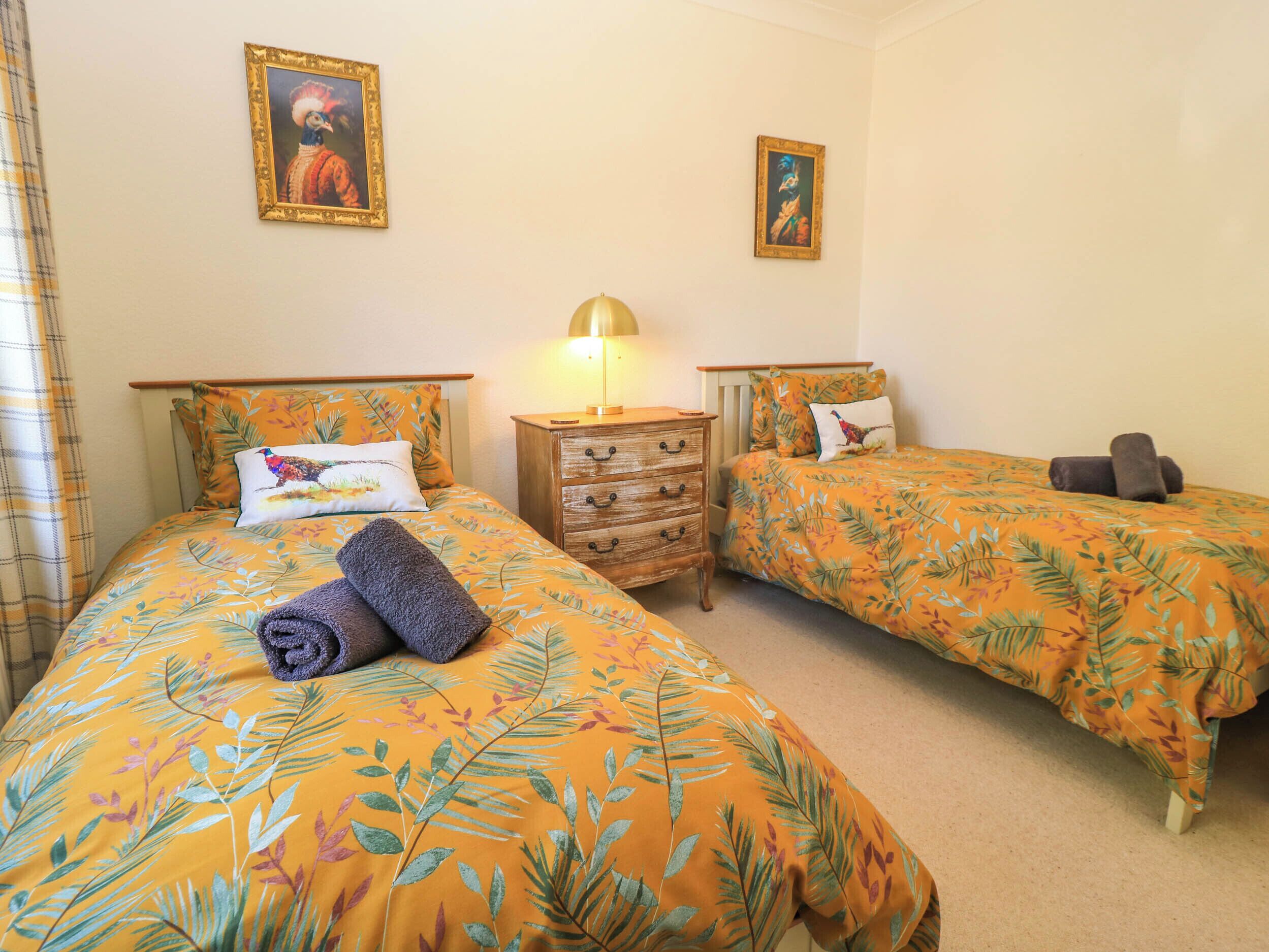 A bedroom with two beds, a nightstand, and a lamp.
