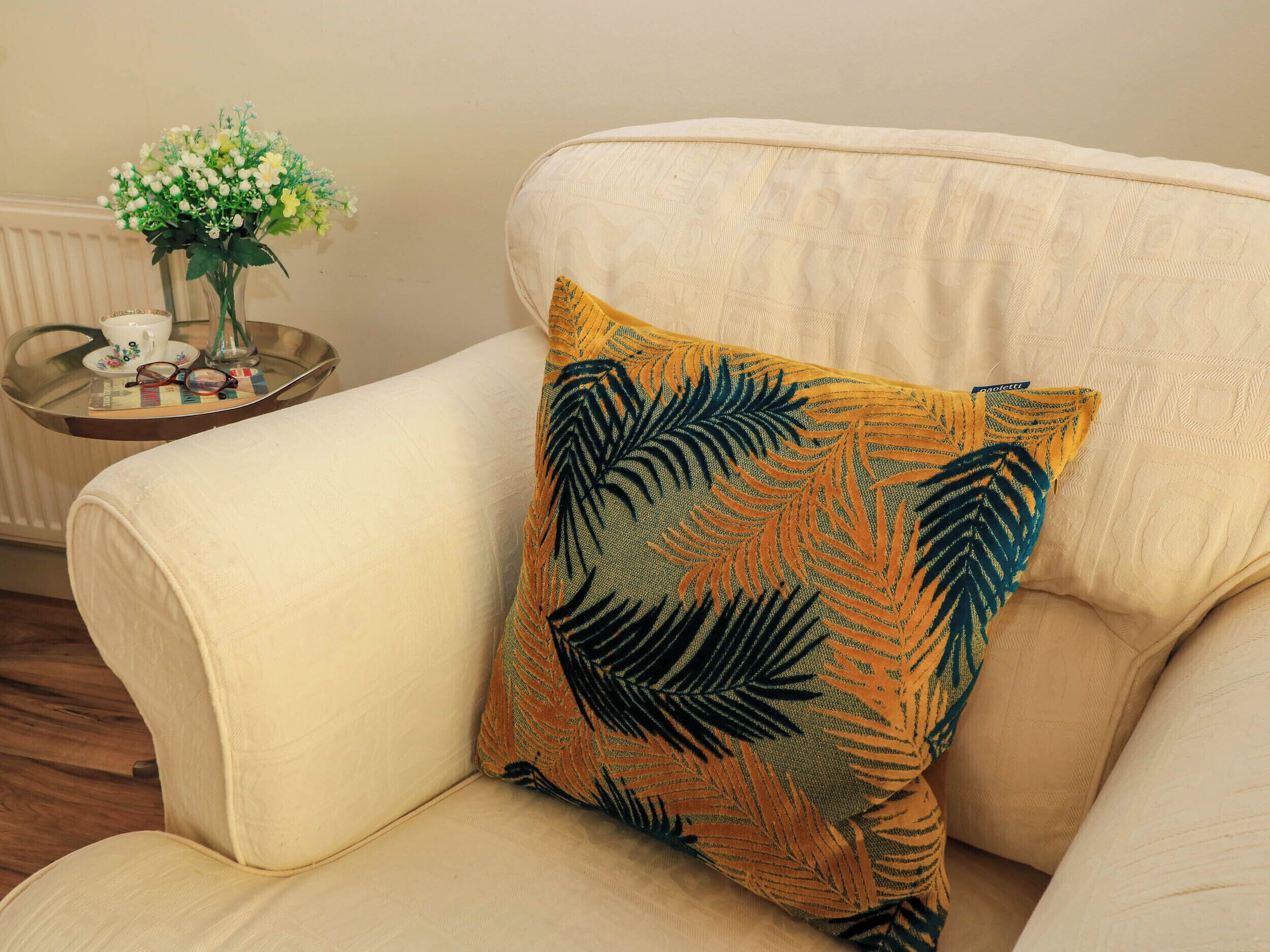 Un fauteuil beige agrémenté d’un coussin décoratif orné d’un motif de feuilles.