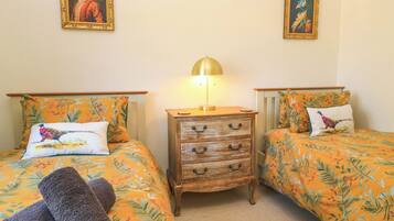 Una habitación con dos camas, cada una con colcha y almohadas a juego con motivos florales. Entre las camas hay una mesita de noche de madera con una lámpara.