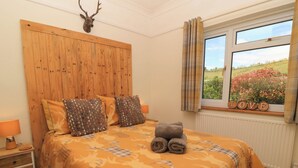 Un dormitorio con cabecera de madera, cama con ropa de cama estampada, ventana con vistas al verdor y una decoración con la palabra 'LOVE' en el alféizar.