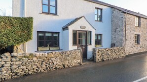 A two-story stone building with a white exterior, a stone wall in front, and a small porch with a door. - Clerk Beck Cottage (Ulverston)