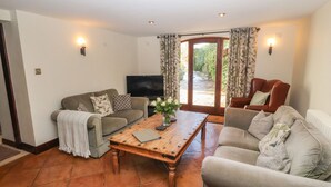 A living room with a sofa, armchair, coffee table, TV, and a door leading to a garden. - Clerk Beck Cottage (Ulverston)