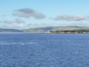 A coastal town with a lighthouse, houses, and hills in the background.