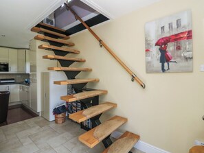 A staircase with wooden steps and a handrail, leading to a kitchen area with cabinets and a refrigerator. - Ettrick Cottage (Rothesay)