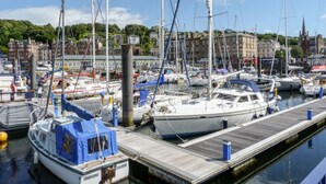 Een jachthaven met meerdere boten die afgemeerd liggen, houten steigers en gebouwen op de achtergrond.