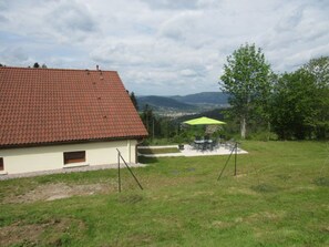 A house with a red-tiled roof, a patio with chairs and a table, and a grassy yard.