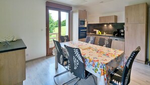 A modern kitchen with a dining area, featuring a table with a floral tablecloth, chairs with patterned upholstery, and a view through a glass door to a garden. - Renovated comfortable house, great view, pets allowed (Gerbamont)