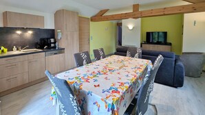 A modern kitchen with wooden cabinets, a dining table with butterfly-patterned tablecloth, and a gray sofa in a living area with a TV. - Renovated comfortable house, great view, pets allowed (Gerbamont)