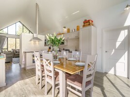 Una cocina moderna con armarios blancos, una mesa de madera para cuatro comensales y un amplio ventanal que proporciona luz natural.