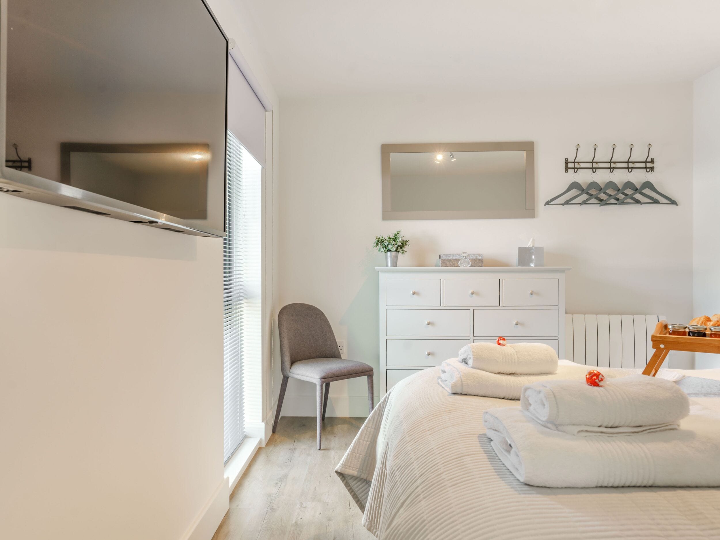 A bedroom with a bed, a chair, a dresser, a mirror, and a coat rack.