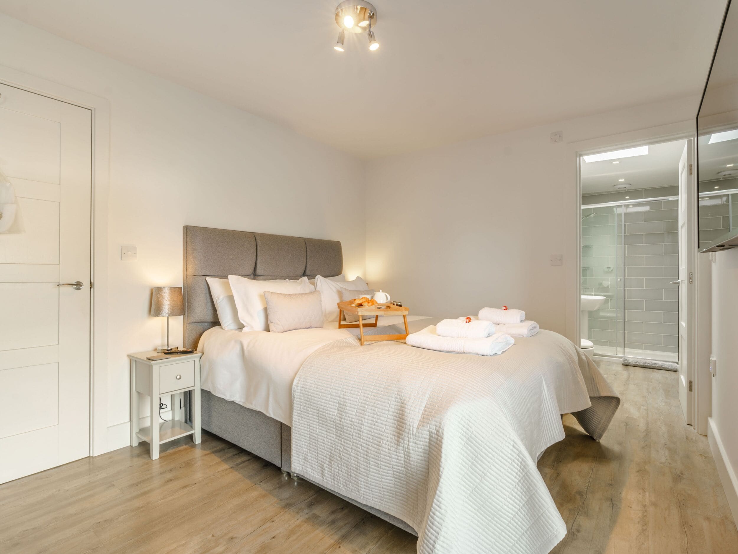 A modern bedroom with a bed, bedside table, and a glass shower area.