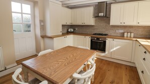 A kitchen with white cabinets, a wooden table, and a stove. - Farriers Cottage (Lincoln)