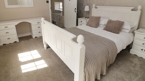 A bedroom with a white bed, a nightstand, a dresser, and a mirror. - Farriers Cottage (Lincoln)