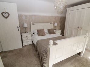 A bedroom with a white bed, two bedside tables, a wardrobe, and a hanging light fixture. - Farriers Cottage (Lincoln)