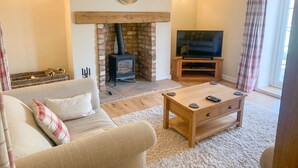 A cozy living room with a fireplace, a sofa, a coffee table, and a TV. - Farriers Cottage (Lincoln)