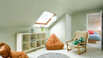 A cozy loft bedroom with a skylight, a white wardrobe, a wooden chair with a fluffy cushion, and a bed with patterned bedding.