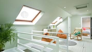 A modern loft bedroom with skylights, a white bed, a chair with a fluffy cushion, and a potted plant.