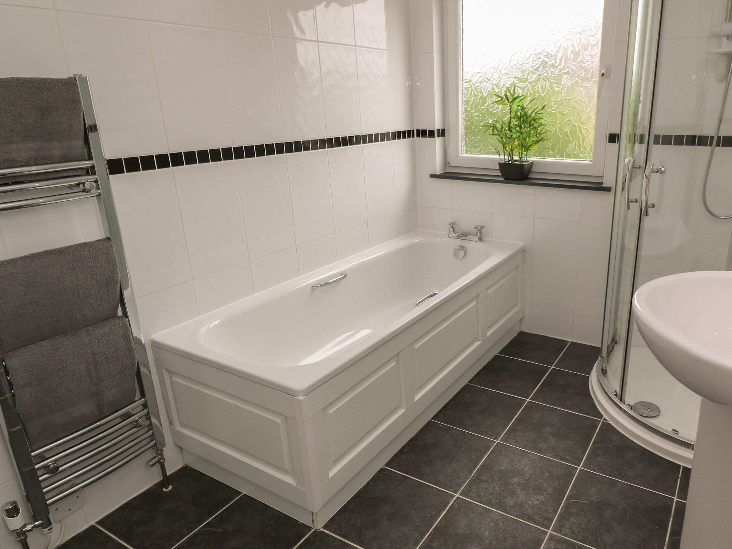 Ein Badezimmer mit einer weißen Badewanne, einer Dusche, einer Toilette und einem Fenster mit einem Blumentopf.