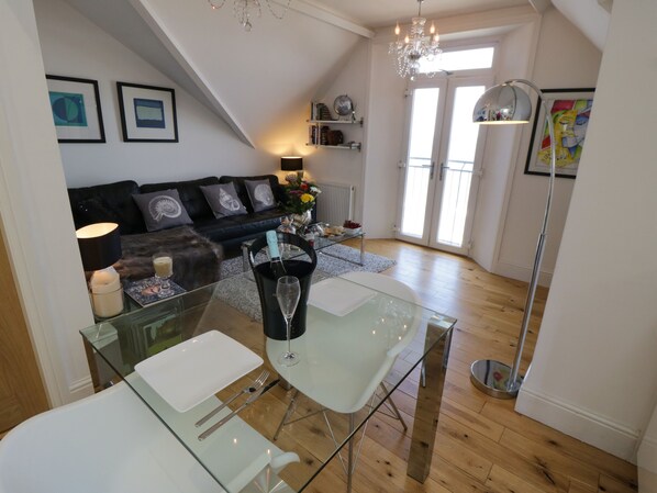 A modern living room with a glass dining table, a black leather sofa, and a chandelier. - Flat 3, Peacehaven (Whitby)