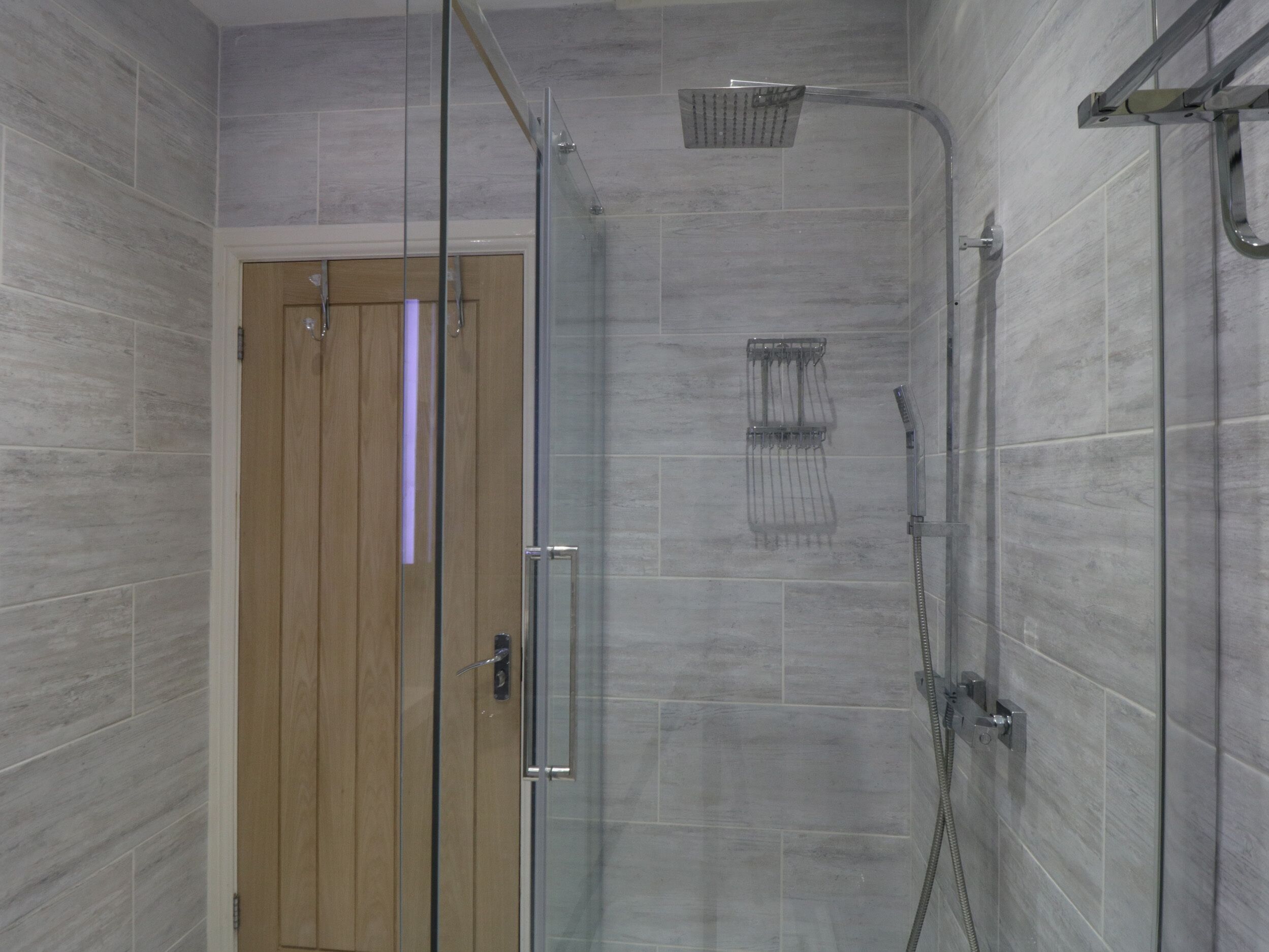 Une douche moderne dotée d’une porte en verre, d’un pommeau de douche à main et d’un pommeau de douche à pluie fixé au mur.