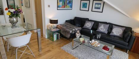 A modern living room with a glass coffee table, a black sofa, and a dining area with a glass table and white chairs.