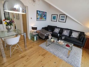 A modern living room with a glass coffee table, a black sofa, and a dining area with a glass table and white chairs.