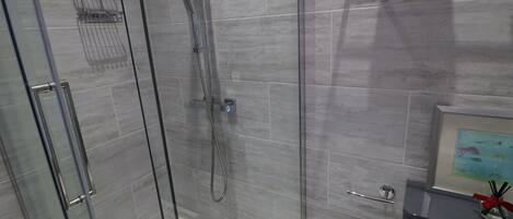 Un baño moderno con cabina de ducha de vidrio, azulejos grises, un cuadro en el tocador y un perchero.