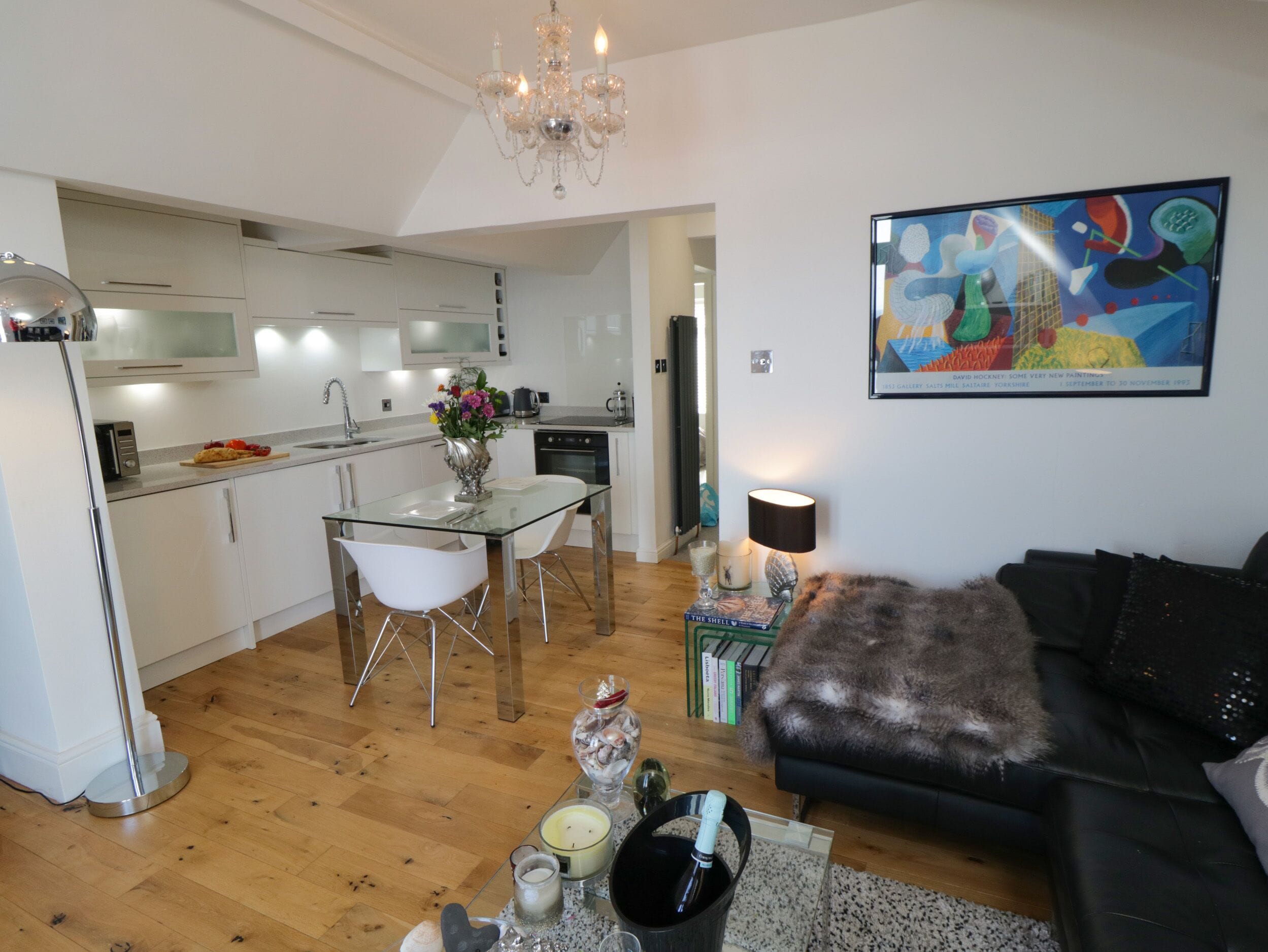 A modern kitchen with white cabinets, a dining area with a glass table, and a living room with a black sofa.