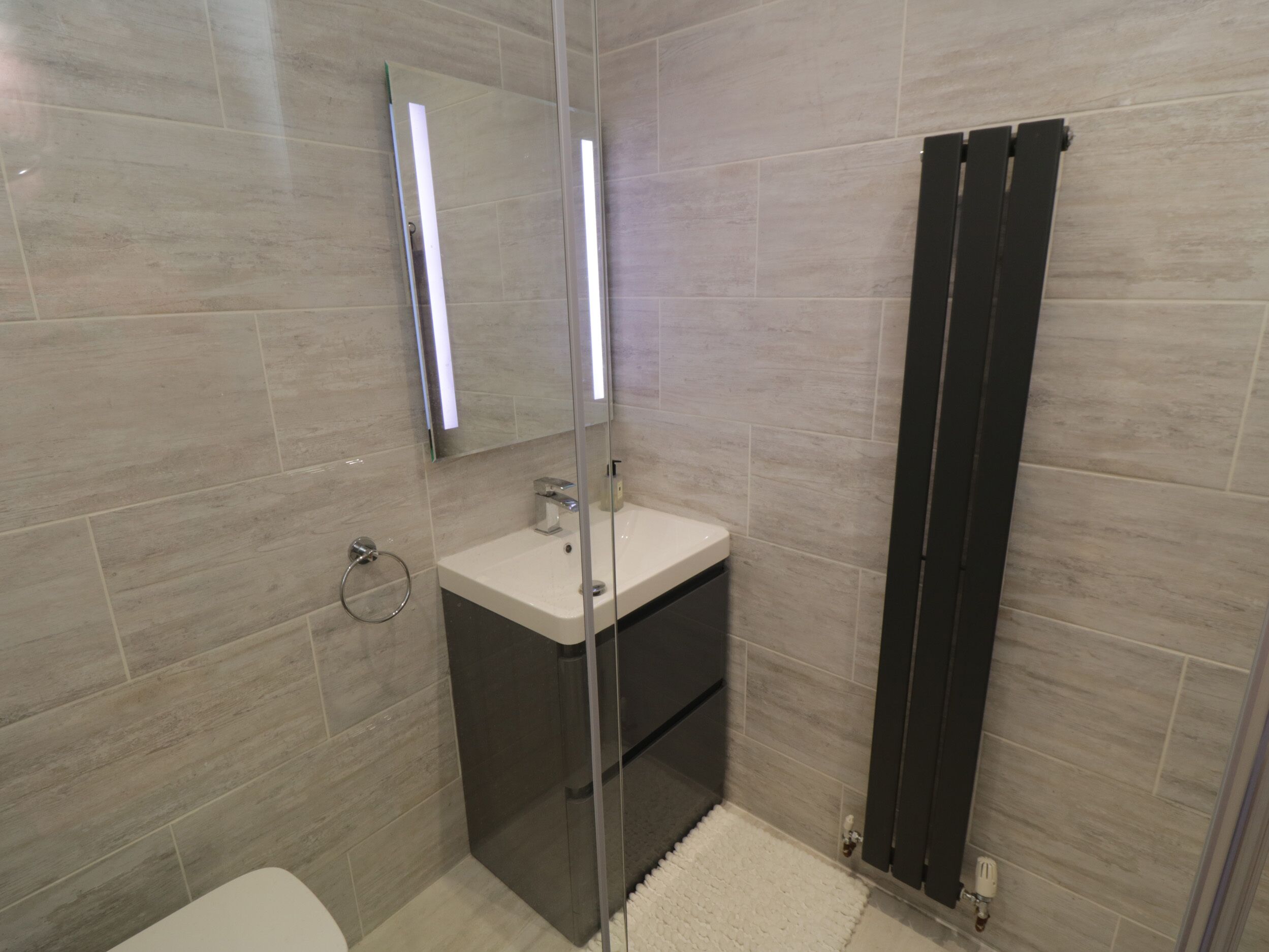 Un bany modern amb una cabina de dutxa de vidre, un envàs de color blanc i un vàter.