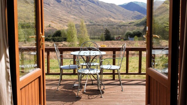 Une terrasse en bois ouverte, avec des chaises et une table en métal, offrant une vue sur un paysage montagneux.