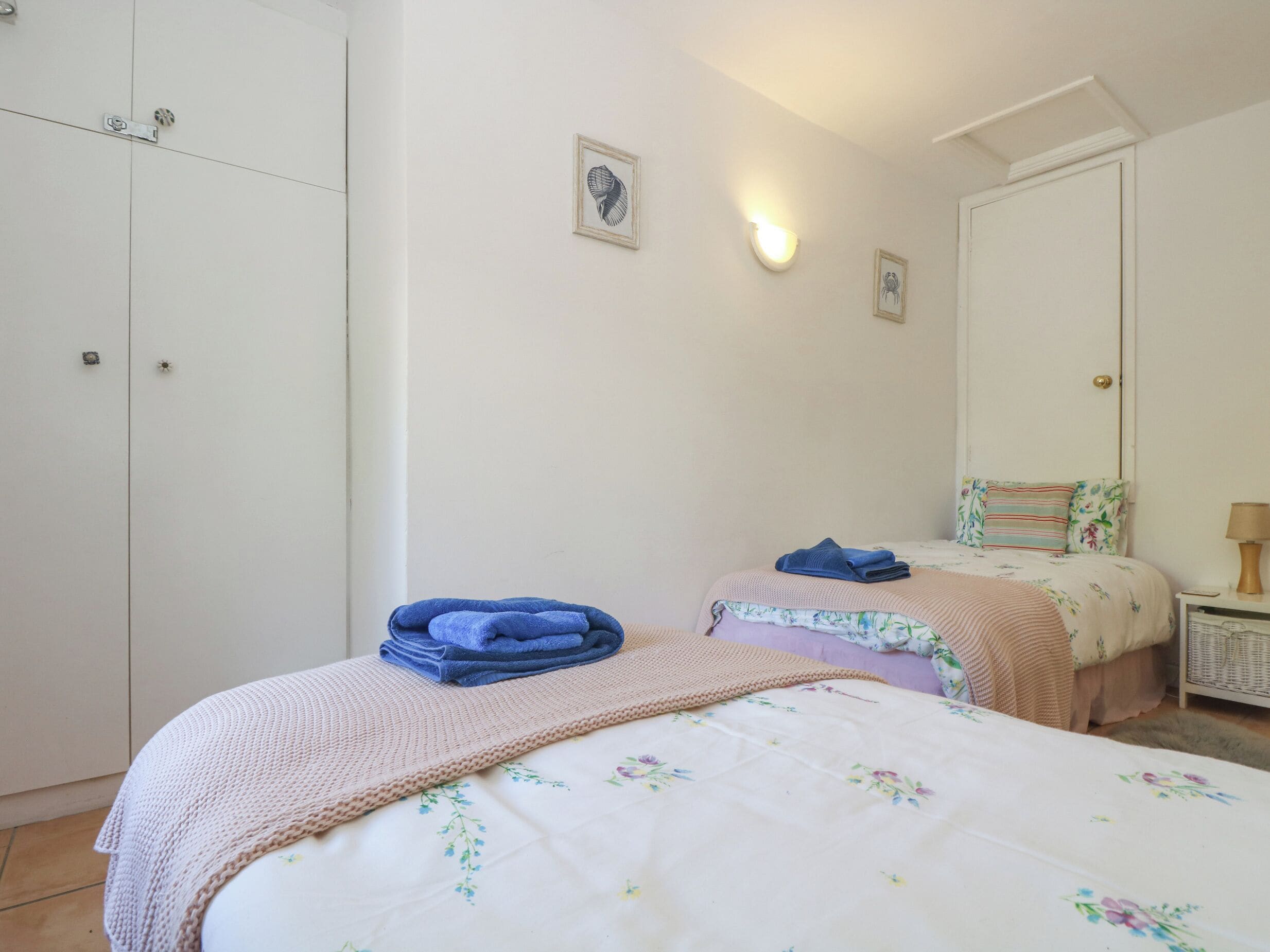 A bedroom with two beds, a wardrobe, and a nightstand with a lamp.