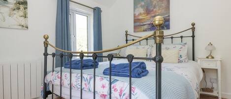 Una cama bien hecha con ropa de cama floral, una mesita de noche con una lámpara y un cuadro en la pared.