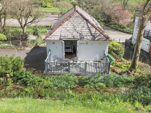 Une petite maison blanche à deux étages, dotée d’un balcon, entourée d’une végétation luxuriante et d’un jardin.
