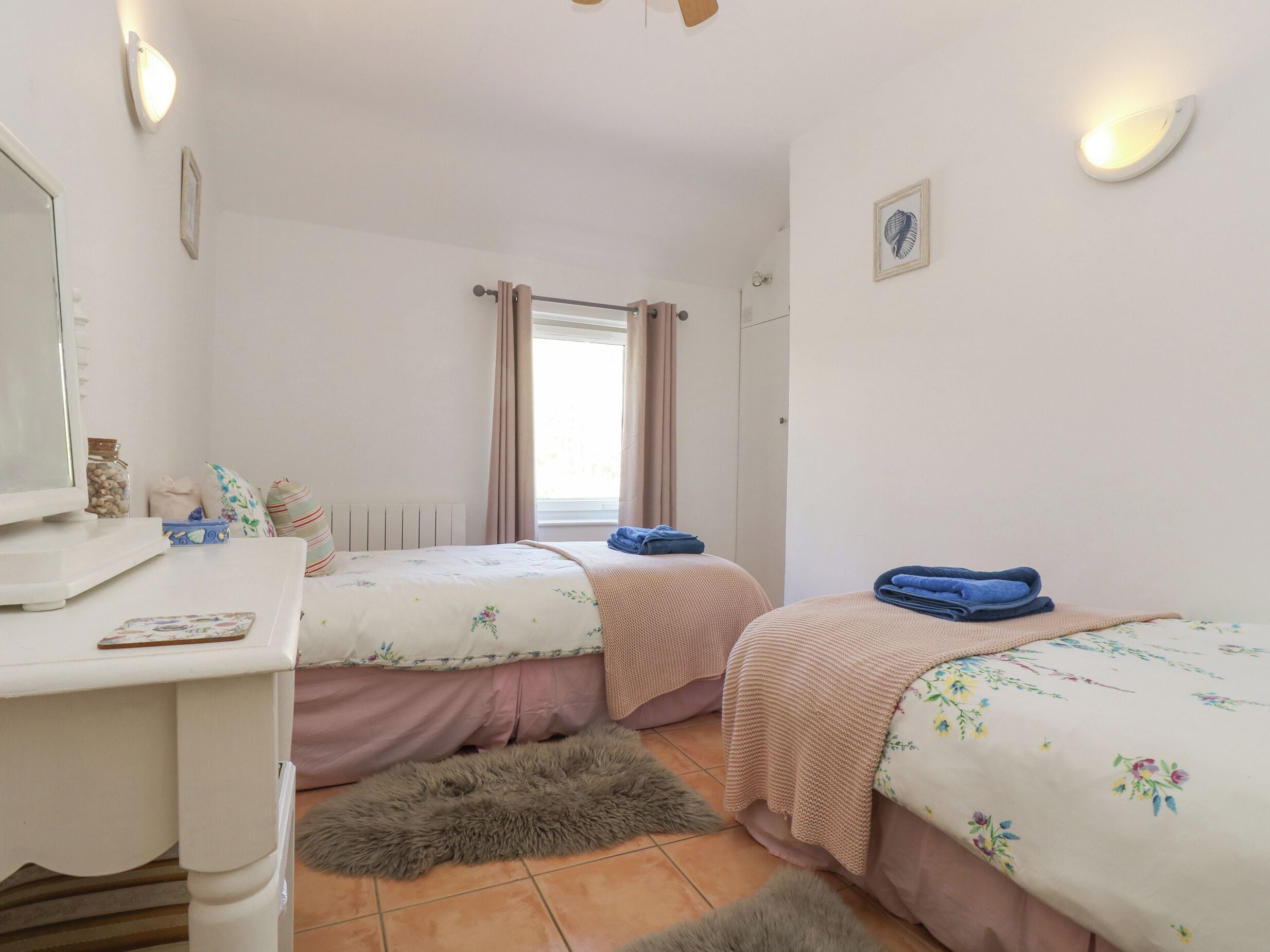 A bedroom with two beds, a desk, a mirror, and a window with curtains.