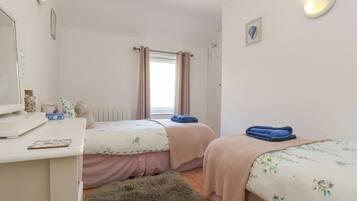 A bedroom with two beds, a desk, a mirror, and a window with curtains.