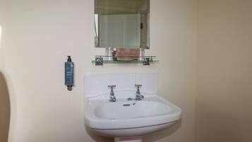 A bathroom with a white sink, two faucets, a glass shelf with a towel, and a mirror above the sink.