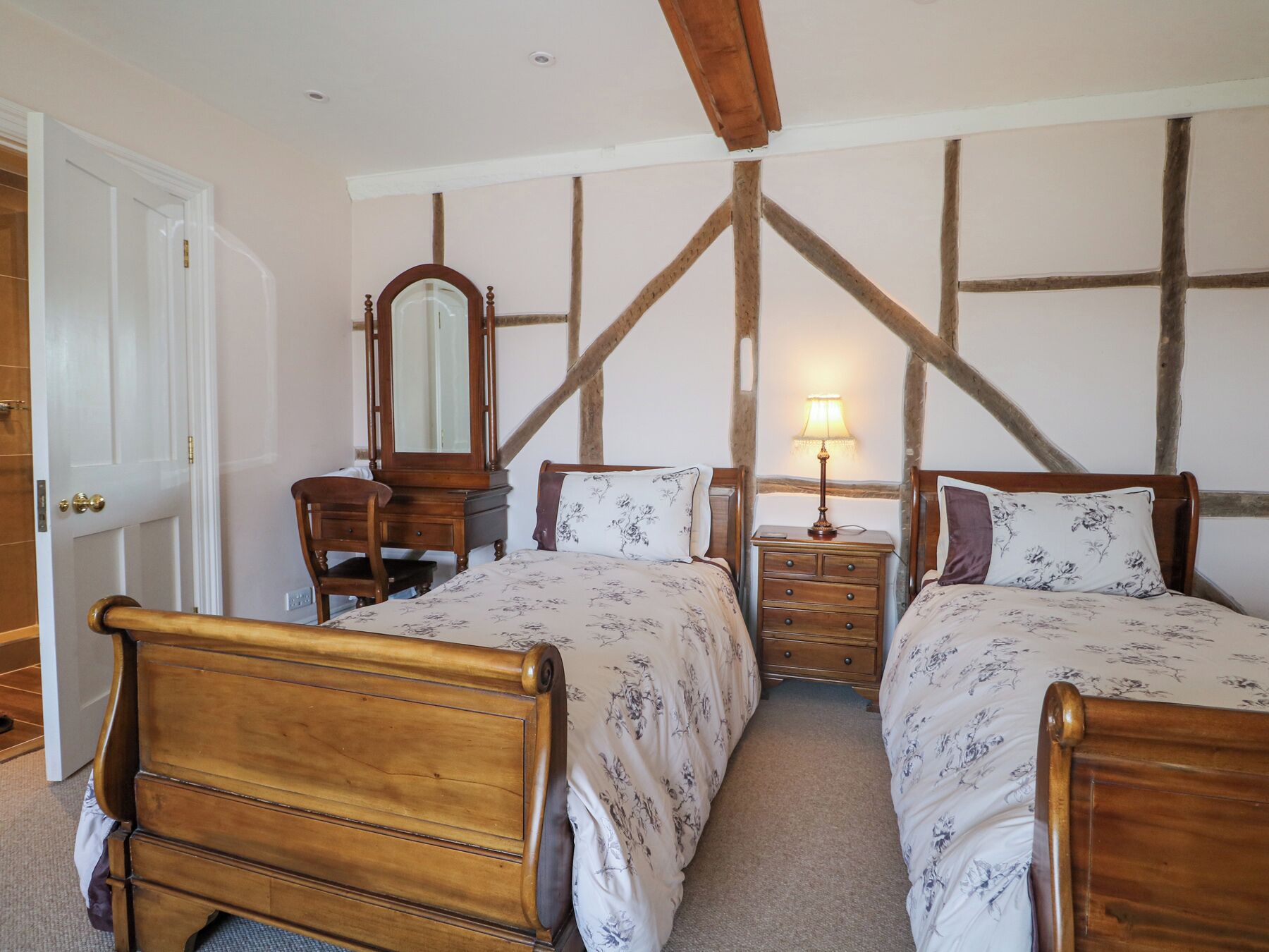 A bedroom with two wooden beds, a wooden dresser, a mirror, and a nightstand with a lamp.
