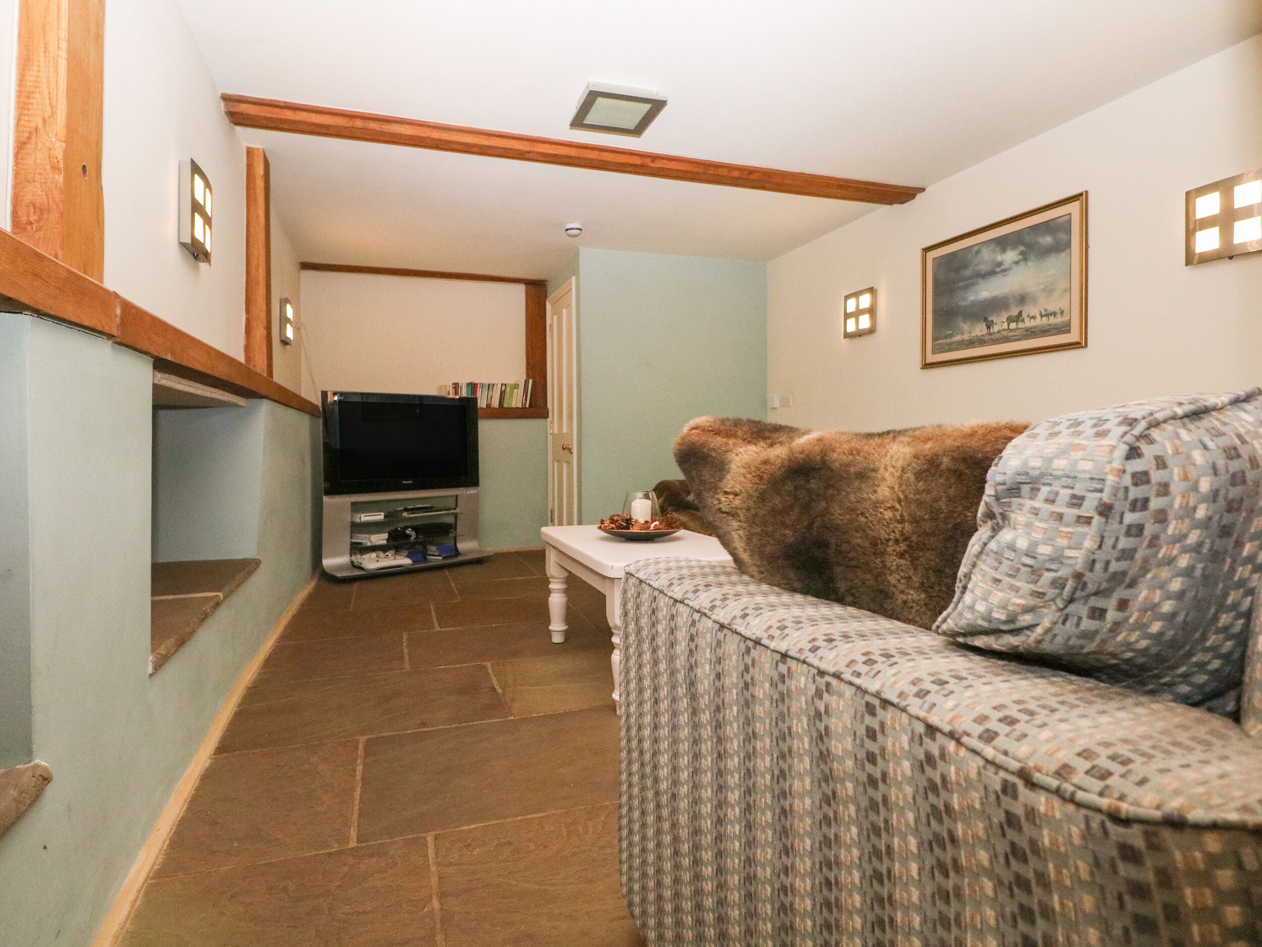 A living room with a television, a patterned sofa, and a painting on the wall.