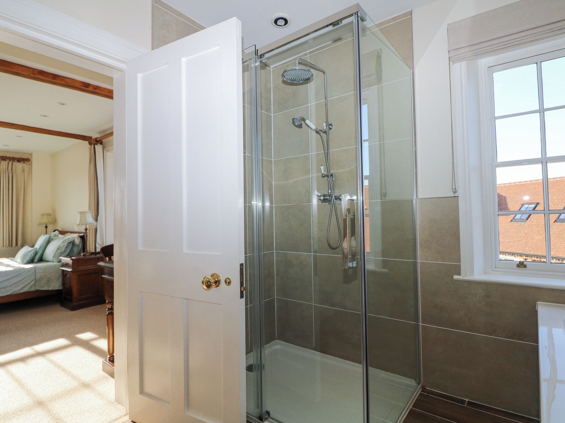 Un baño moderno con ducha envuelta en vidrio, una puerta blanca y vistas al exterior a través de una ventana.