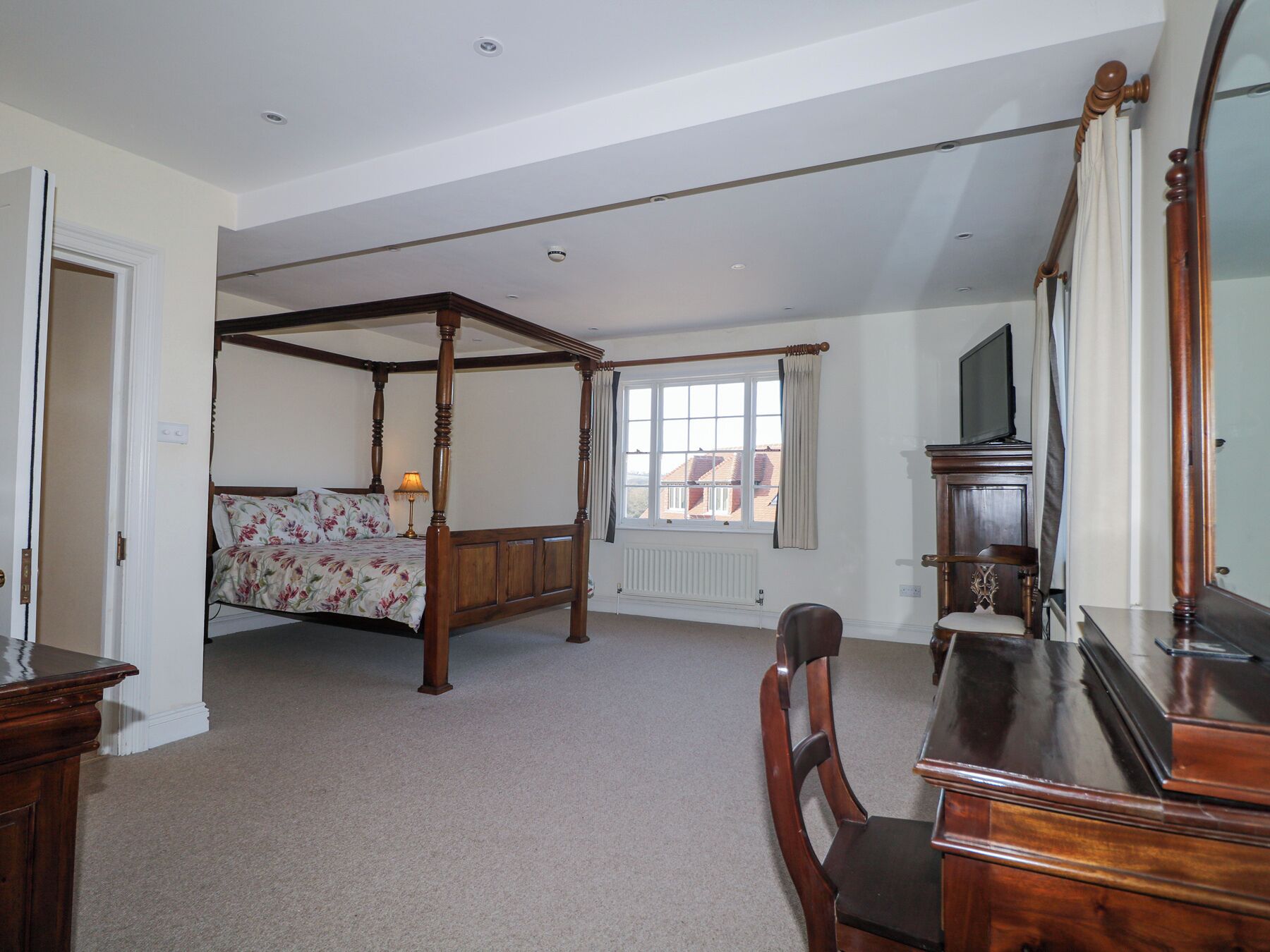 A bedroom with a four-poster bed, a desk with a mirror, and a television.