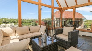 A spacious patio with wicker furniture, a glass table, and a view of a red-roofed building. - Groomes Country House (Bordon)