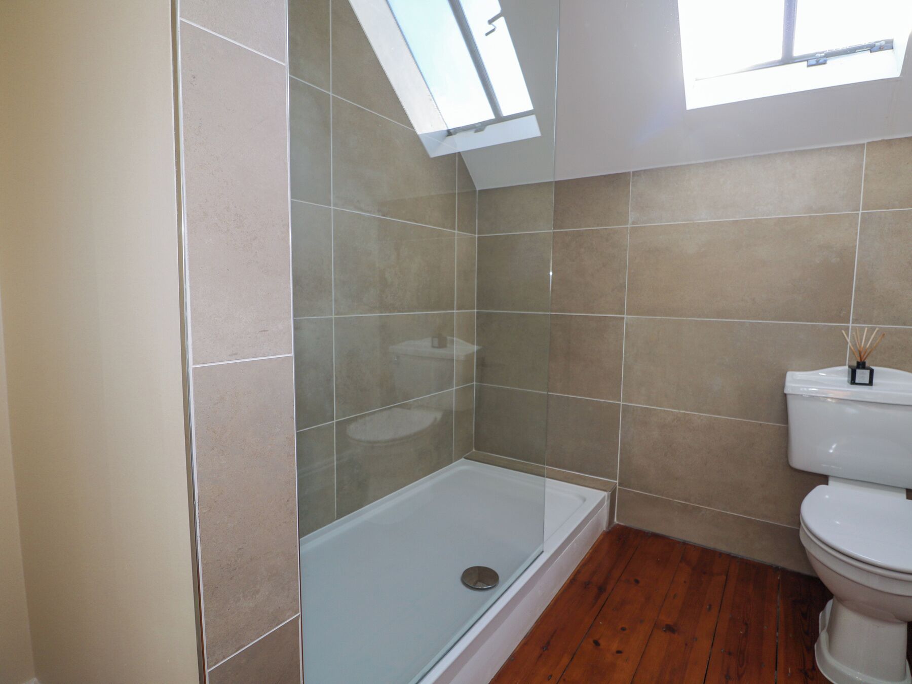 Une salle de bain dotée d’une douche à parois de verre, de toilettes et d’un puits de lumière.