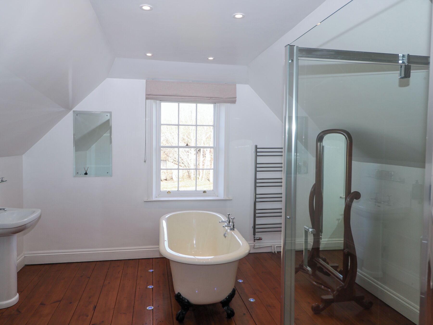 A bathroom with a freestanding bathtub, a glass shower enclosure, a toilet, and a window with a view of trees.