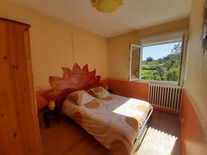 A bedroom with a bed, a window with a view of greenery, and a radiator.