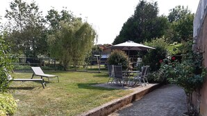 Ein gepflasterter Weg führt zu einer Terrasse mit Gartenmöbeln und einem überdachten Sitzbereich.