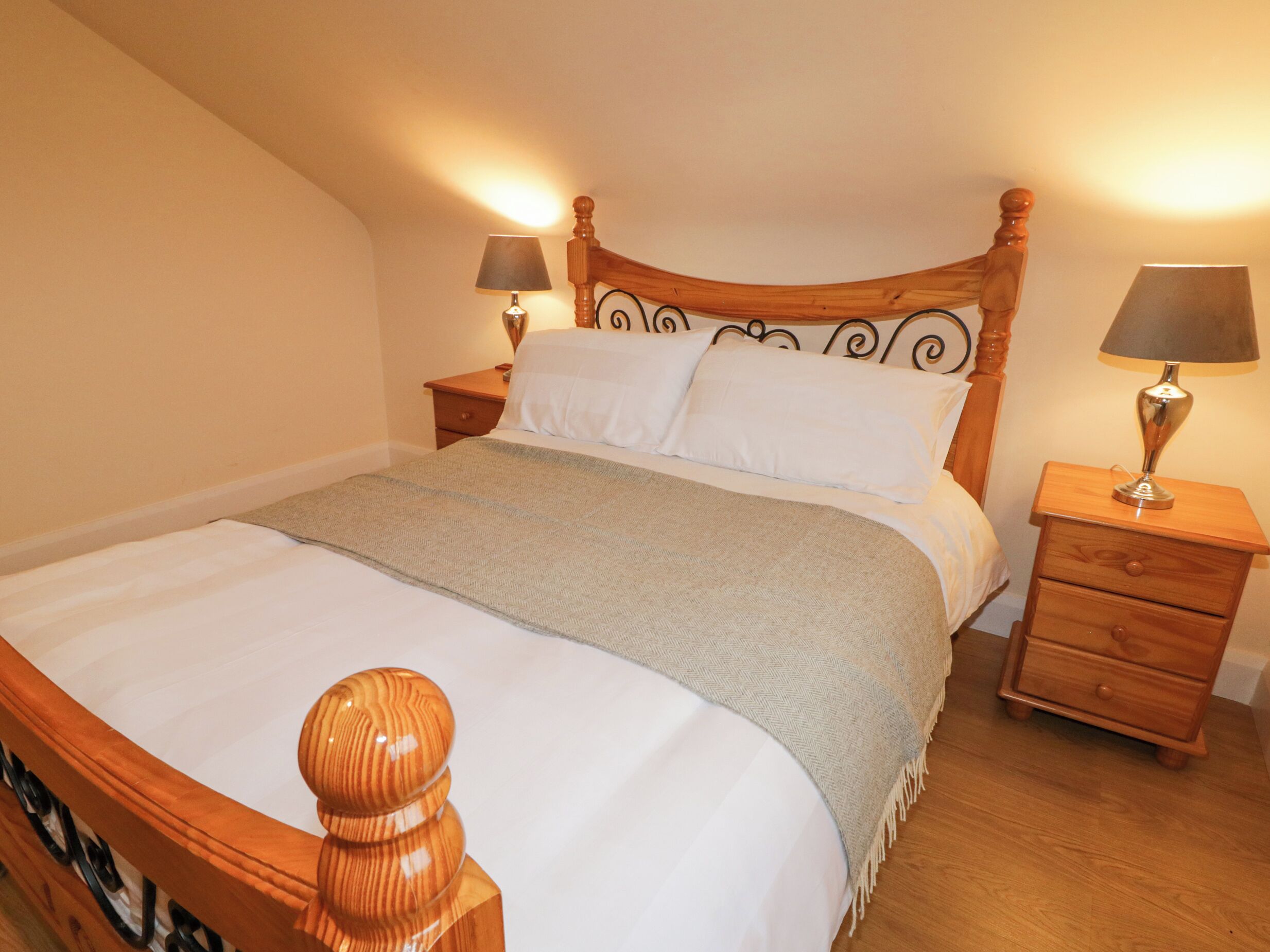 Una cama bien hecha con tablero de madera, dos mesitas de noche con lámparas y una manta de diseño espiga.