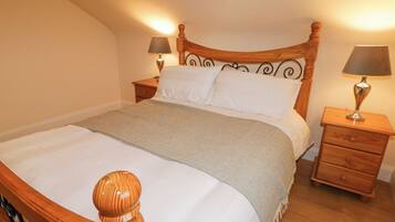 Una cama bien hecha con tablero de madera, dos mesitas de noche con lámparas y una manta de diseño espiga.