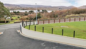 A fenced area with a road curving around it, a grassy field, and a body of water in the background.