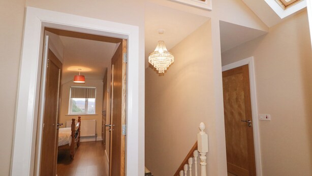 A hallway with a wooden floor, a staircase with white balusters, a chandelier, and a door leading to another room.